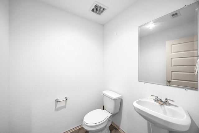 half bath featuring visible vents, toilet, baseboards, and a sink