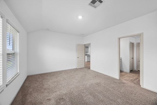 unfurnished bedroom featuring light colored carpet, vaulted ceiling, visible vents, and baseboards