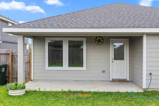 property entrance with a patio area, roof with shingles, and fence
