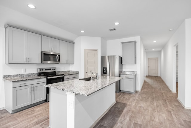 kitchen with light stone counters, a sink, stainless steel appliances, light wood finished floors, and visible vents