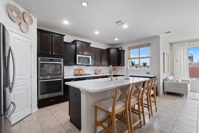 kitchen with a sink, visible vents, a kitchen bar, appliances with stainless steel finishes, and light tile patterned floors