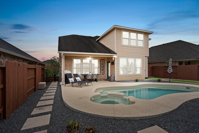 back of house at dusk with a patio area, a pool with connected hot tub, and a fenced backyard