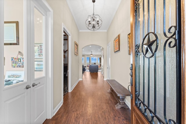 foyer featuring arched walkways, dark wood-style flooring, baseboards, a chandelier, and crown molding