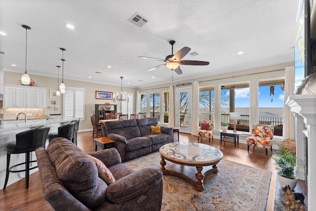 living area featuring ornamental molding, wood finished floors, visible vents, and ceiling fan with notable chandelier
