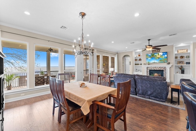 dining room with ceiling fan with notable chandelier, a glass covered fireplace, recessed lighting, and dark wood finished floors