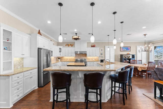 kitchen with a chandelier, gas range, white cabinets, under cabinet range hood, and freestanding refrigerator