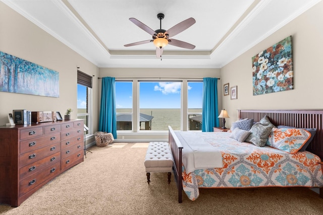bedroom featuring a tray ceiling, a water view, crown molding, carpet flooring, and ceiling fan