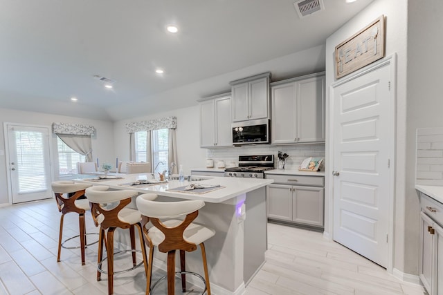 kitchen with an island with sink, stainless steel appliances, visible vents, tasteful backsplash, and a breakfast bar area