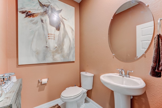 half bath featuring toilet, baseboards, and a sink