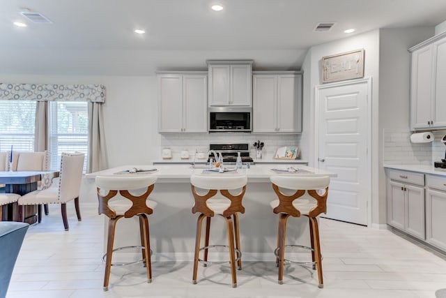 kitchen with a kitchen breakfast bar, decorative backsplash, range, stainless steel microwave, and visible vents
