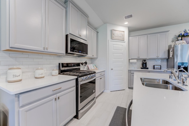kitchen with a sink, decorative backsplash, stainless steel appliances, light countertops, and visible vents