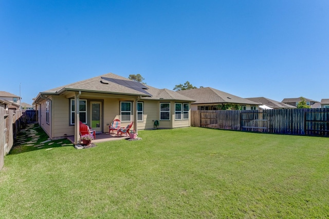back of property featuring a fenced backyard, a shingled roof, solar panels, a patio, and a lawn