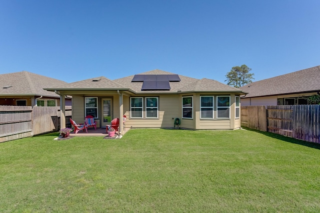 rear view of property featuring a fenced backyard, roof mounted solar panels, a yard, and a patio