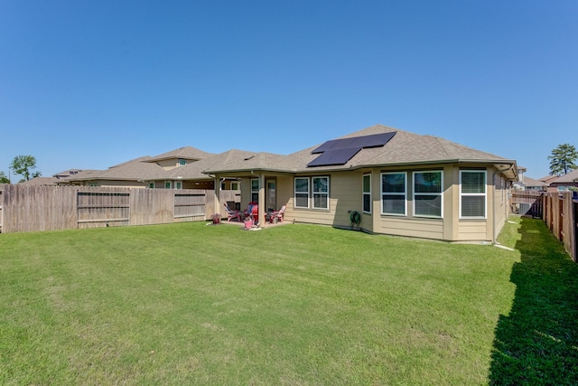 back of property featuring a fenced backyard, roof mounted solar panels, and a yard