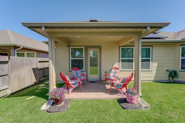 rear view of property featuring roof mounted solar panels, a patio area, a lawn, and fence