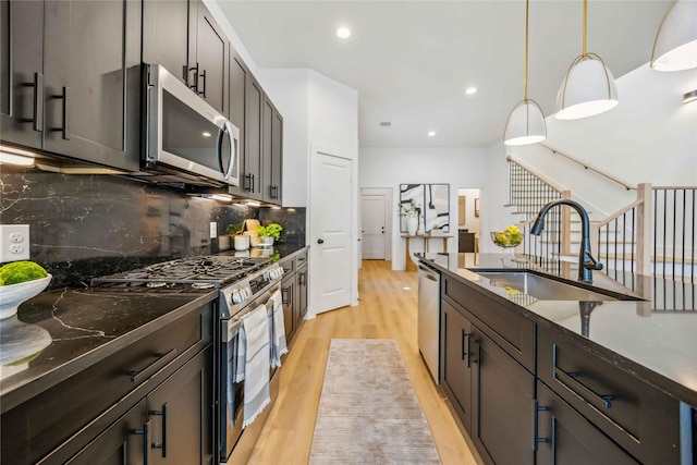 kitchen featuring decorative backsplash, pendant lighting, a sink, light wood-style flooring, and stainless steel appliances