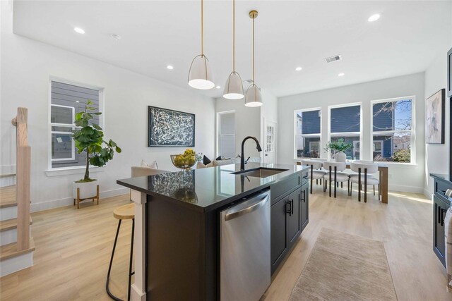 kitchen with a sink, light wood finished floors, dishwasher, baseboards, and a center island with sink
