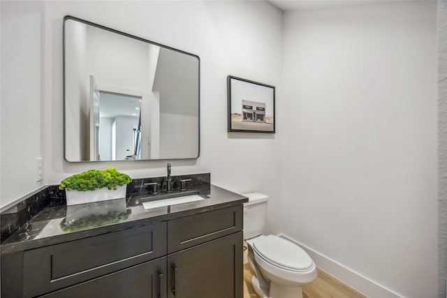 half bathroom with toilet, baseboards, wood finished floors, and vanity