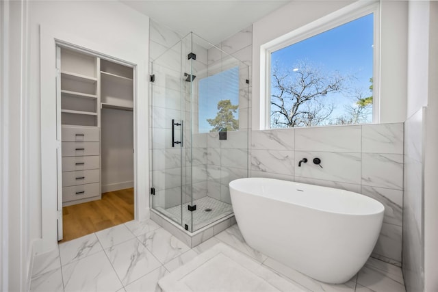 full bathroom featuring a spacious closet, a freestanding bath, marble finish floor, and a stall shower