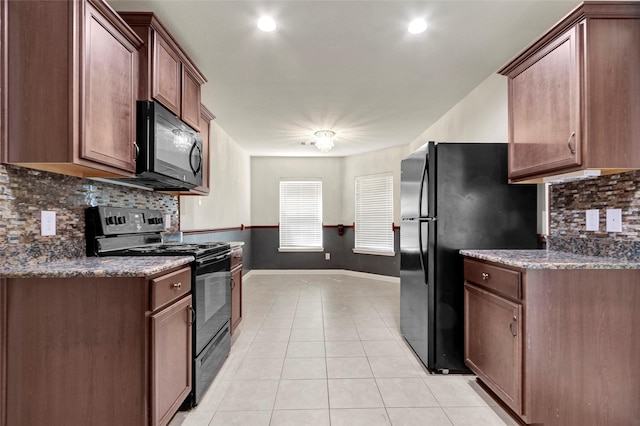 kitchen featuring dark stone countertops, tasteful backsplash, light tile patterned flooring, baseboards, and black appliances