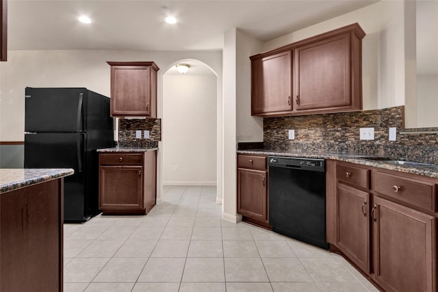 kitchen with dark stone counters, black appliances, light tile patterned floors, arched walkways, and backsplash