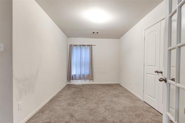 carpeted empty room featuring baseboards, visible vents, and a textured ceiling