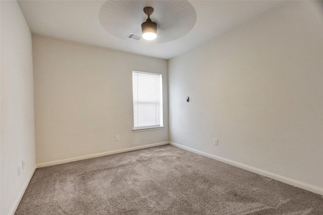 carpeted spare room featuring baseboards, visible vents, and ceiling fan