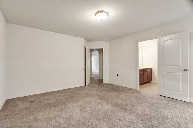 unfurnished bedroom with baseboards, ensuite bath, and light colored carpet