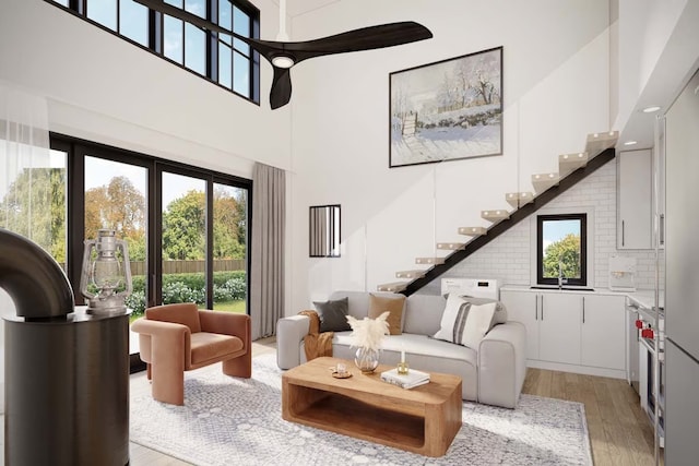living area with stairway, a towering ceiling, and light wood-style flooring