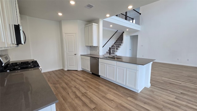 kitchen featuring a peninsula, a sink, dark countertops, visible vents, and appliances with stainless steel finishes