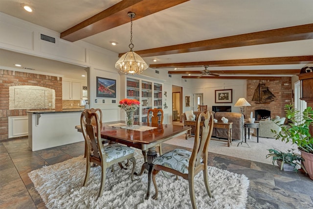 11831 Thoreau Dr, Montgomery, TX 77356 - dining space with beamed ceiling, stone tile flooring, a brick fireplace, brick wall, and ceiling fan with notable chandelier