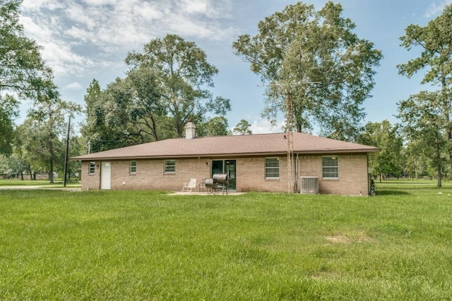 rear view of property with brick siding, a patio area, a lawn, and a chimney
