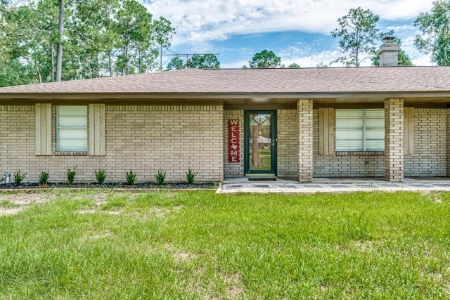 single story home featuring a chimney, a front lawn, brick siding, and a shingled roof