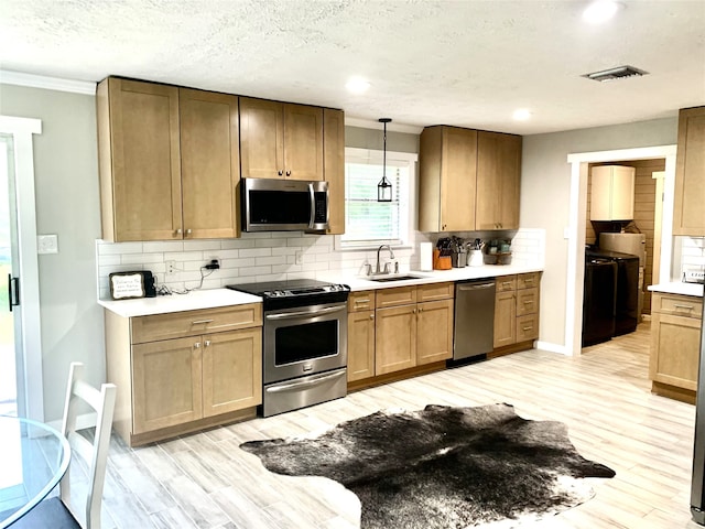 kitchen with tasteful backsplash, a sink, light wood finished floors, washing machine and dryer, and appliances with stainless steel finishes