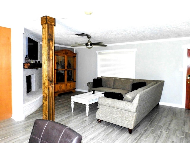 living room with wood finished floors, a ceiling fan, baseboards, a textured ceiling, and a large fireplace