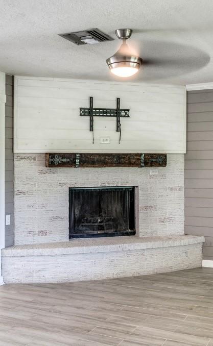 room details featuring a textured ceiling, wood finished floors, wooden walls, a fireplace, and visible vents