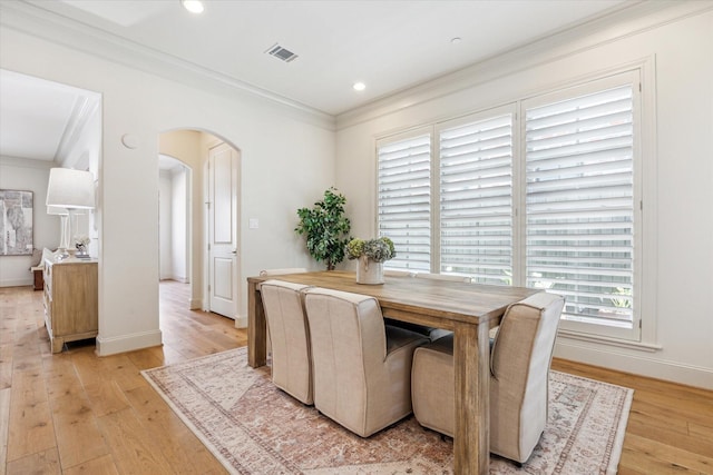 dining space featuring light wood-style flooring, arched walkways, and crown molding