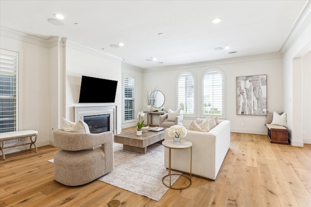 living room with a glass covered fireplace, visible vents, light wood-style floors, and crown molding