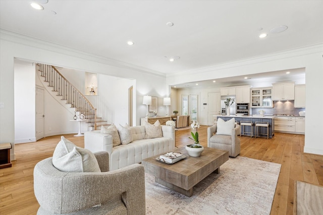 living area with recessed lighting, light wood finished floors, crown molding, and stairs