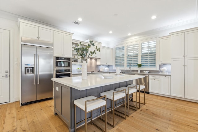 kitchen with stainless steel appliances, visible vents, decorative backsplash, a kitchen bar, and light wood-style flooring