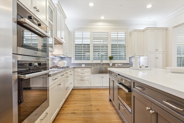 kitchen featuring white cabinets, a sink, light wood-style floors, crown molding, and light countertops