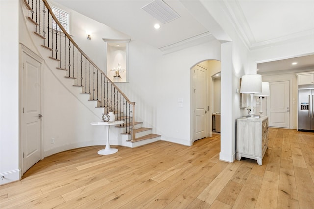 foyer featuring stairway, crown molding, light wood-style floors, arched walkways, and visible vents