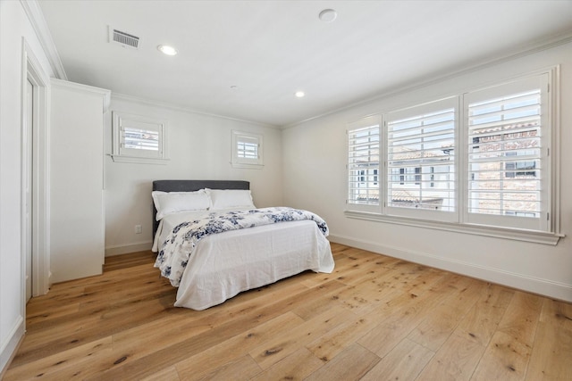 bedroom with light wood-type flooring, baseboards, visible vents, and ornamental molding
