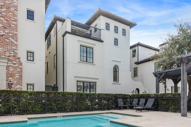 back of property featuring fence, a community pool, a balcony, and stucco siding