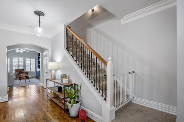 stairs with baseboards, arched walkways, wood finished floors, and ornamental molding