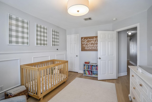 bedroom with visible vents, light wood finished floors, and a crib