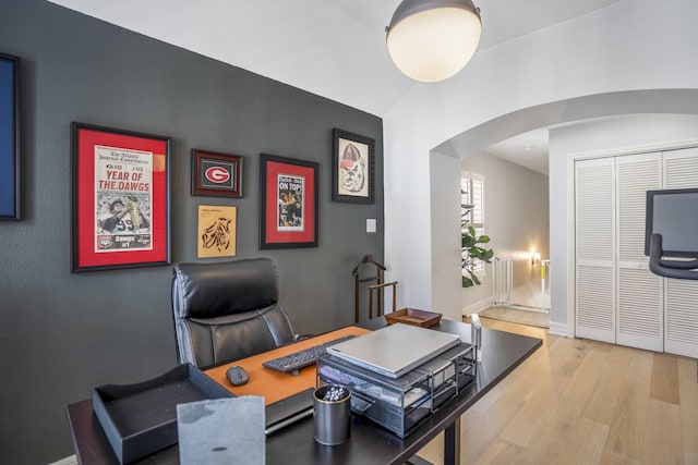 office area with arched walkways, baseboards, wood finished floors, and radiator