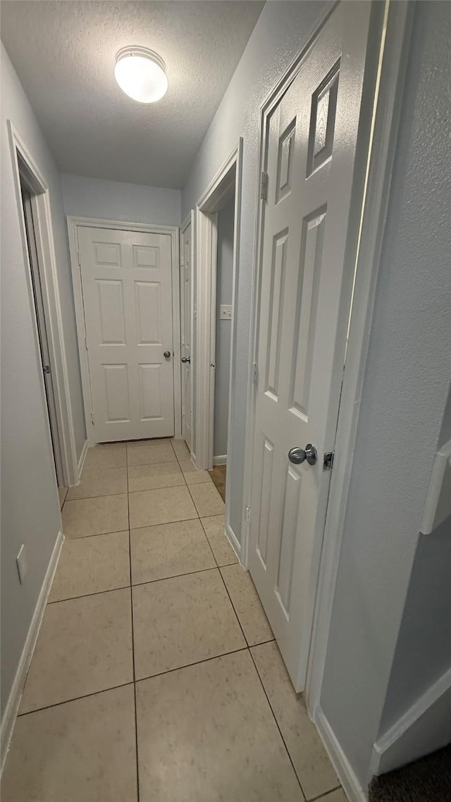 hallway with baseboards, light tile patterned flooring, and a textured ceiling