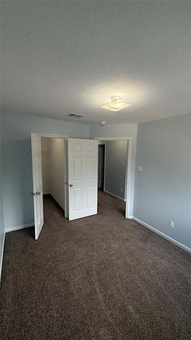 unfurnished bedroom featuring dark carpet, a textured ceiling, and baseboards