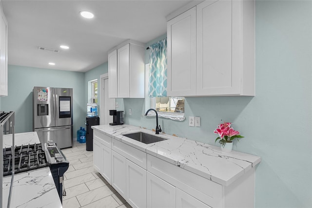 kitchen featuring white cabinets, a sink, stainless steel fridge, recessed lighting, and light stone counters